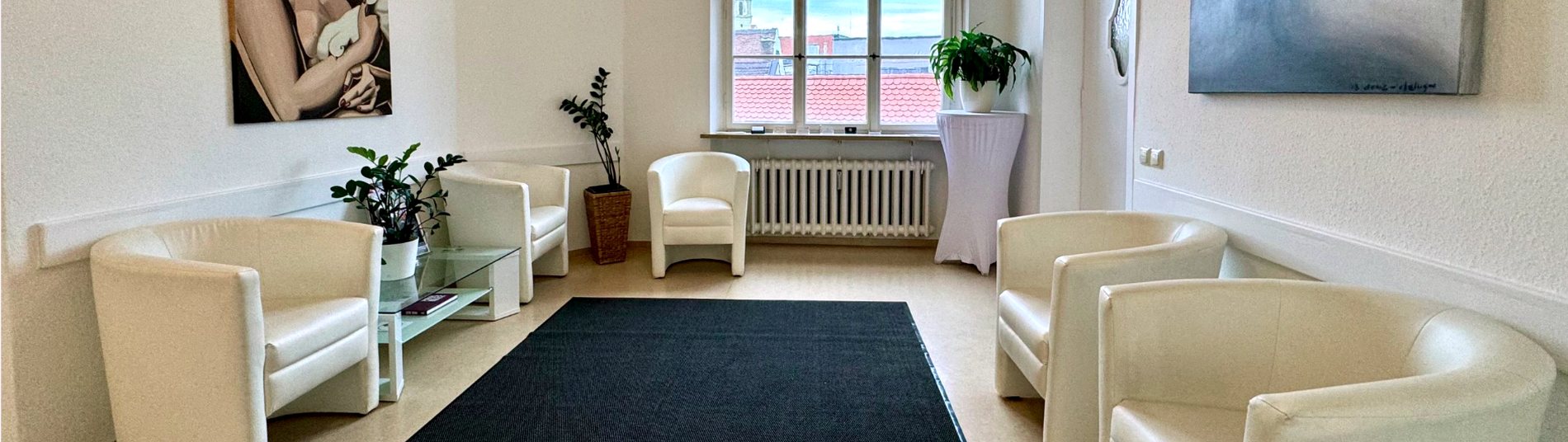 Heller Empfangsraum der Gemeinschaftspraxis mit cremefarbenen Sesseln und Blick über die Dächer der Augsburger Altstadt