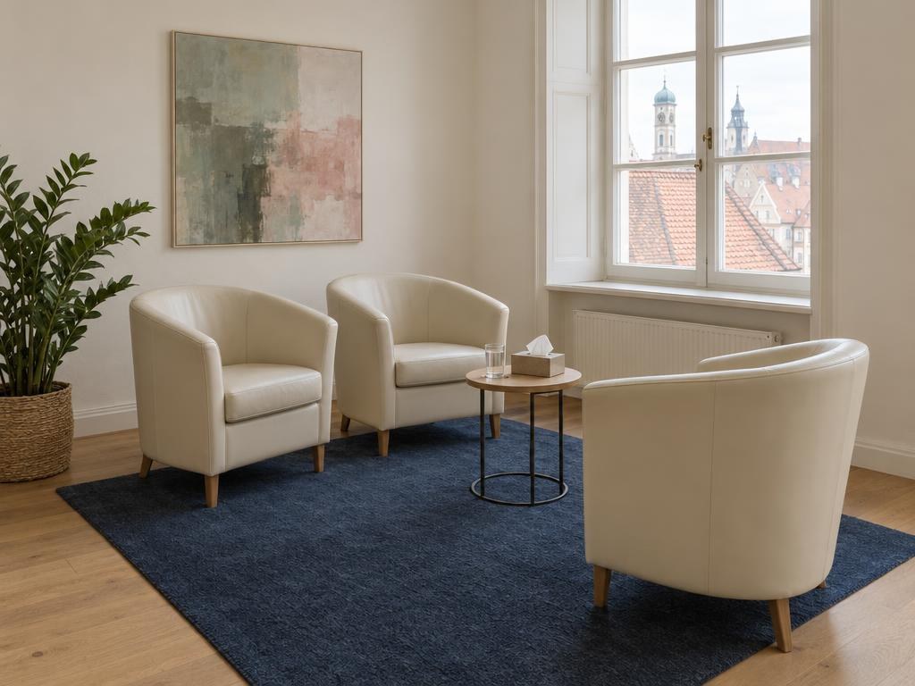 Heller Beratungsraum mit drei cremefarbenen Sesseln auf einem dunkelblauen Teppich und Blick über die Dächer der Altstadt